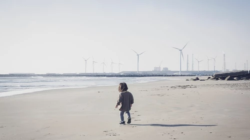 Child walking in the beach close to wind farm