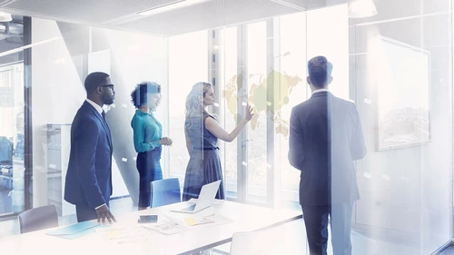 Group of people standing in modern meeting room and looking at a virtual map of the world